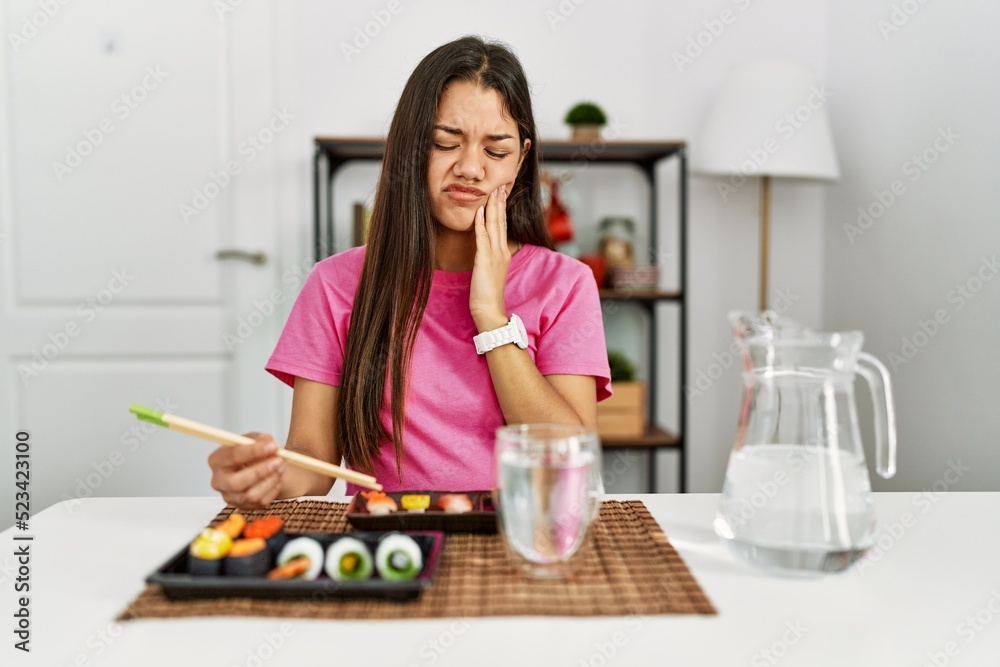 Young brunette woman eating sushi using chopsticks touching mouth with hand with painful expression because of toothache or dental illness on teeth. dentist concept. Young brunette woman eating sushi using chopsticks touching mouth with hand with painful expression because of toothache or dental illness on teeth. dentist concept.