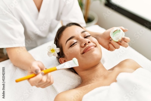 Young latin woman relaxed having skin face aloe vera treatment at beauty center