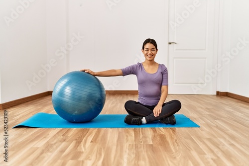 Young latin woman smiling confident stretching using fit ball at sport center