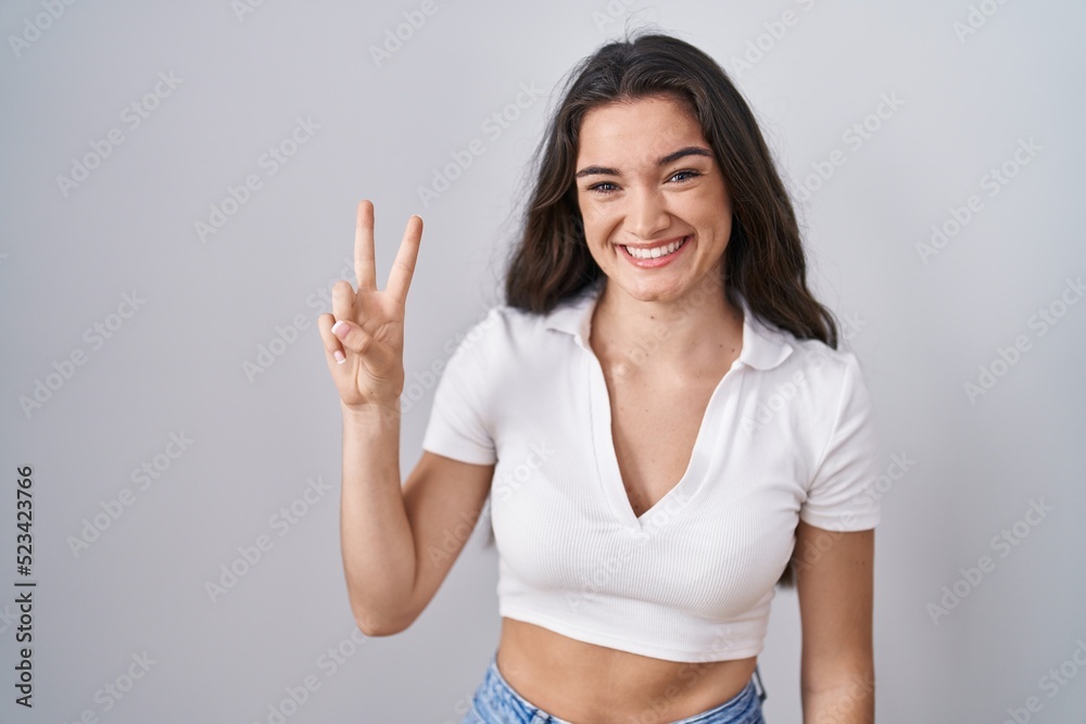 Young teenager girl standing over white background showing and pointing up with fingers number two while smiling confident and happy.