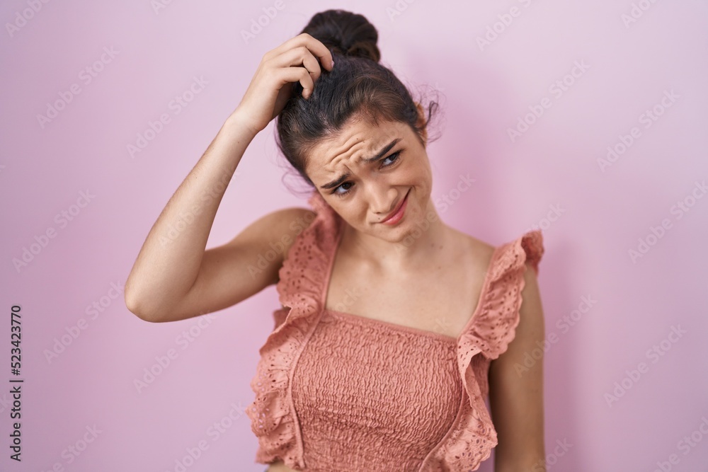 Young teenager girl standing over pink background confuse and wonder about question. uncertain with doubt, thinking with hand on head. pensive concept. Young teenager girl standing over pink background confuse and wonder about question. uncertain with doubt, thinking with hand on head. pensive concept.