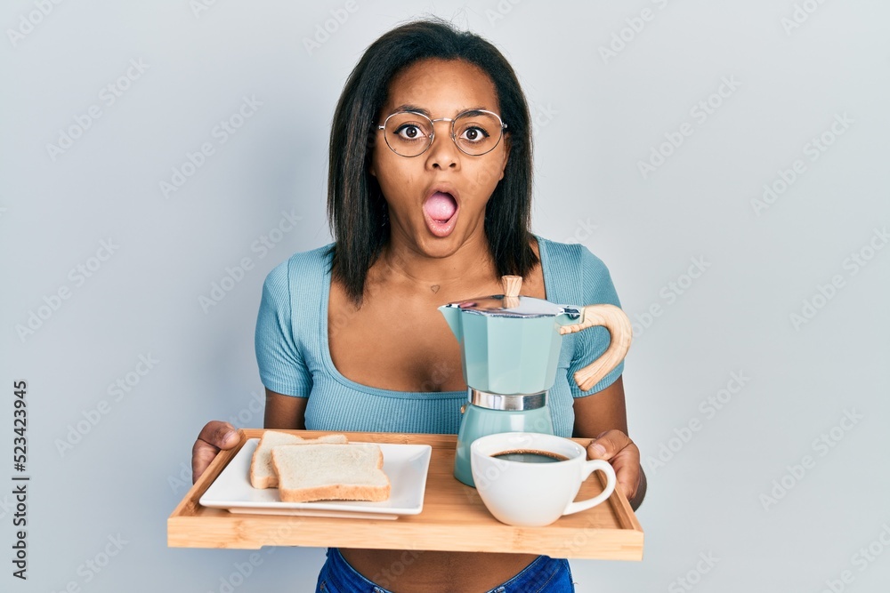 Young african american girl holding tray with breakfast food afraid and shocked with surprise and amazed expression, fear and excited face.