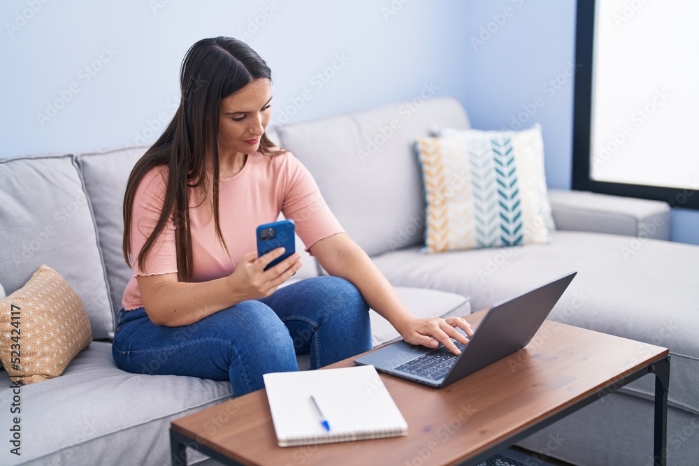 Young beautiful hispanic woman using smartphone and laptop at home Young beautiful hispanic woman using smartphone and laptop at home