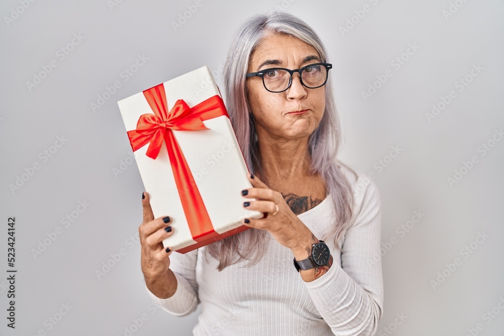 Middle age woman with grey hair holding gift puffing cheeks with funny face. mouth inflated with air, catching air. Middle age woman with grey hair holding gift puffing cheeks with funny face. mouth inflated with air, catching air.