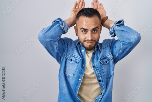 Young hispanic man standing over isolated background doing bunny ears gesture with hands palms looking cynical and skeptical. easter rabbit concept. photo