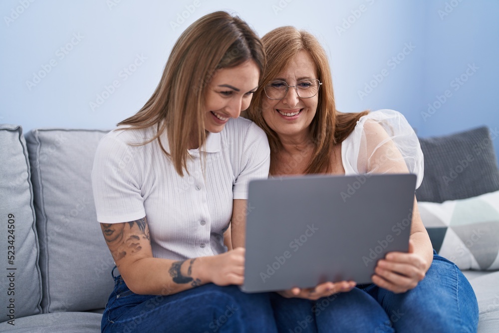 Mother and daughter using laptop sitting on sofa at home Mother and daughter using laptop sitting on sofa at home