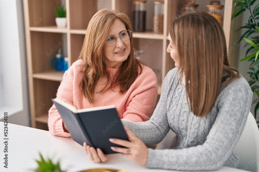 Mother and daughter reading book sitting on desk at home Mother and daughter reading book sitting on desk at home