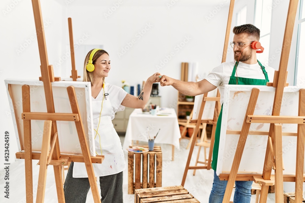 Young caucasian couple smiling happy listening to music and bump fists at art studio.