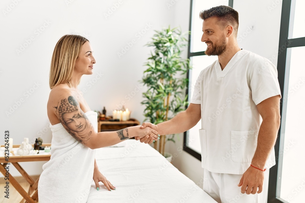 Obraz premium Young caucasian woman at physiotherapy clinic getting muscle massage by professional therapist. Physiotherapist man shaking hands with client