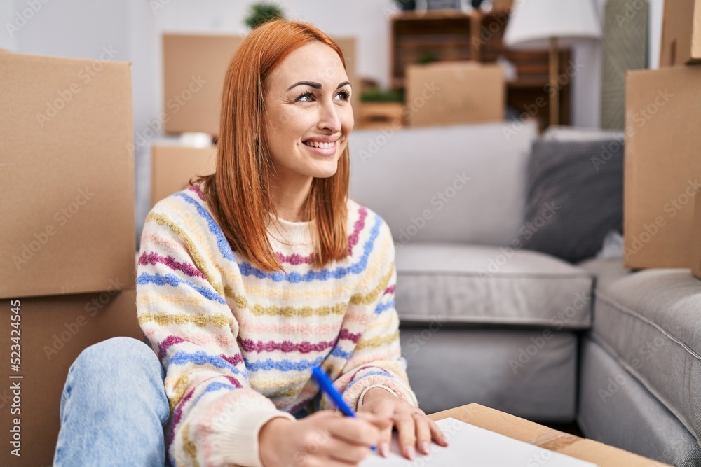 Young caucasian woman smiling confident writing on notebook at new home Young caucasian woman smiling confident writing on notebook at new home