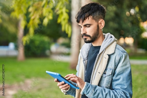 Young hispanic man using touchpad standing at park
