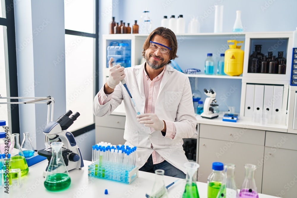 Handsome middle age man working at scientist laboratory with angry face, negative sign showing dislike with thumbs down, rejection concept Handsome middle age man working at scientist laboratory with angry face, negative sign showing dislike with thumbs down, rejection concept
