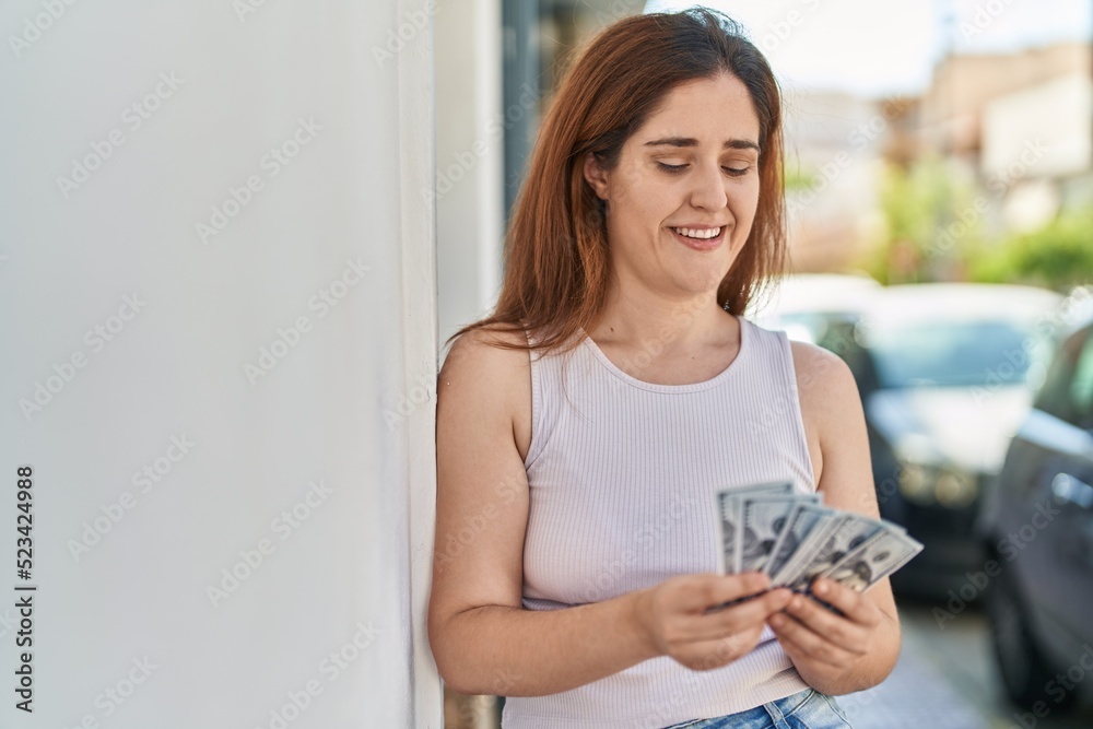 Young woman smiling confident counting dollars at street