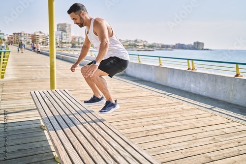 Hispanic man working out jumping a bench outdoors on a sunny day
