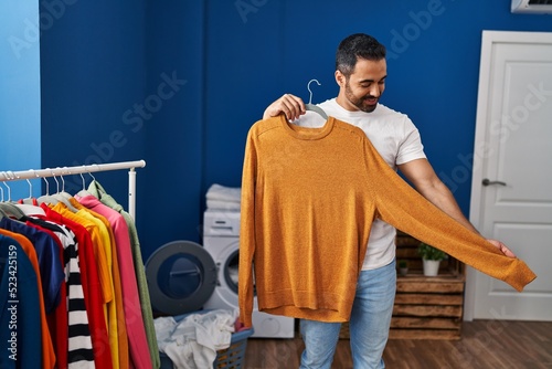Young hispanic man holding sweater at laundry room