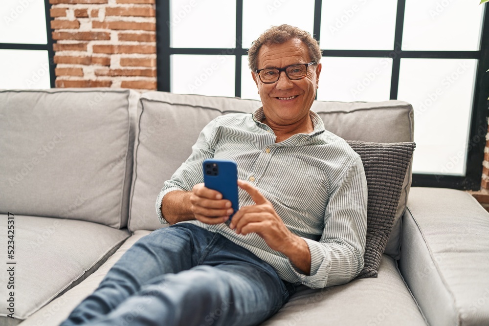 Middle age man using smartphone sitting on sofa at home Middle age man using smartphone sitting on sofa at home