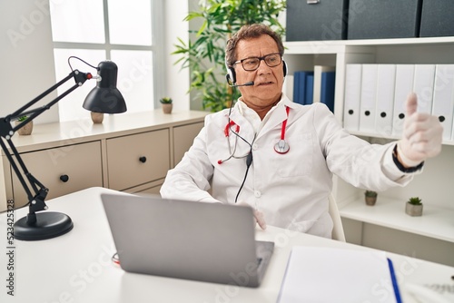 Senior doctor man working on online appointment looking proud  smiling doing thumbs up gesture to the side