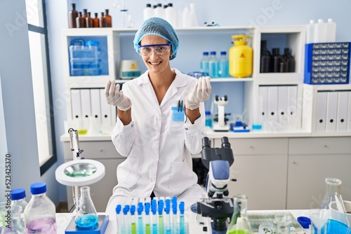 Brunette woman working at scientist laboratory doing money gesture with hands, asking for salary payment, millionaire business