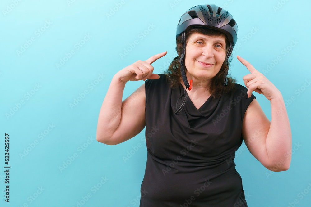 A happy woman wearing a bicycle and pointing her finger on a helmet on a blue background. Bicyclist. Bike. Biker. Biking. Blue. Care. Control. Crash. Cycling. Cycling Helmet. Cyclist. Defense A happy woman wearing a bicycle and pointing her finger on a helmet on a blue background. Bicyclist. Bike. Biker. Biking. Blue. Care. Control. Crash. Cycling. Cycling Helmet. Cyclist. Defense