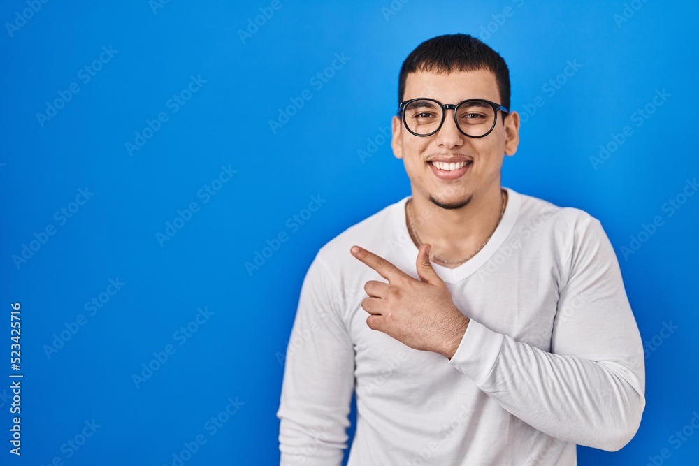 Fototapeta premium Young arab man wearing casual white shirt and glasses cheerful with a smile of face pointing with hand and finger up to the side with happy and natural expression on face