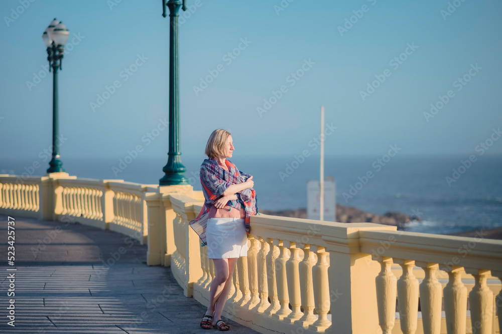 A woman with a backpack stands on the promenade by the sea.