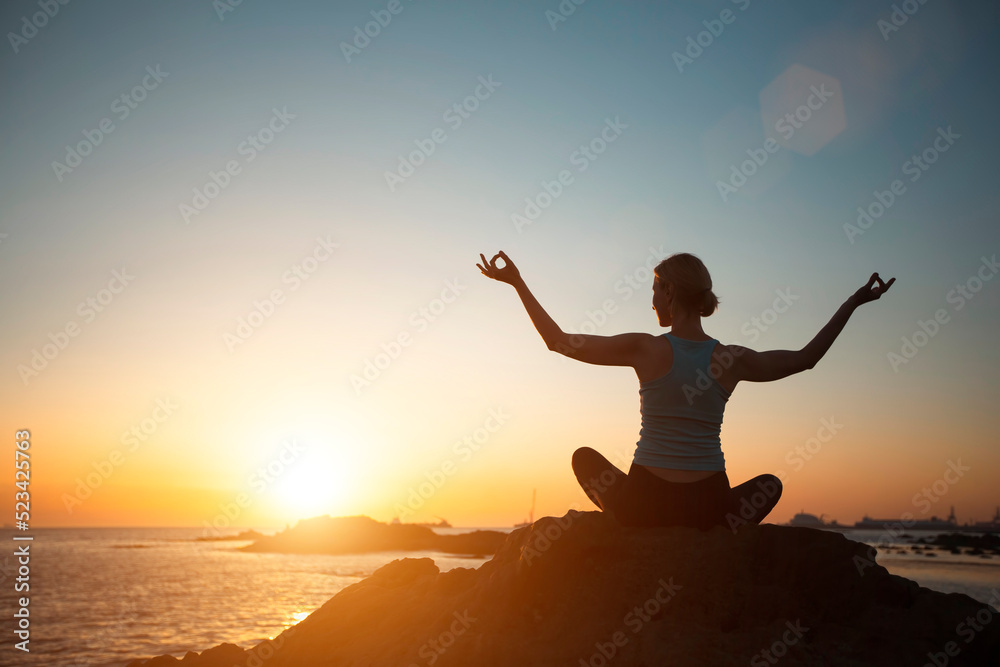 A woman of athletic build does yoga, meditating on the ocean beach during a beautiful sunset.