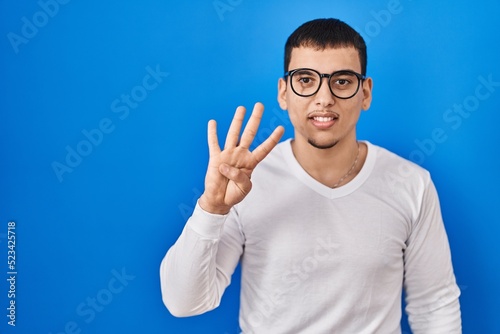 Young arab man wearing casual white shirt and glasses showing and pointing up with fingers number four while smiling confident and happy.