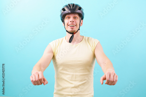 A man wearing a bicycle helmet simulates driving on a bicycle on a blue background. Hobbies. Tool. Protector. Activity. Adult. Background. Bicycle. Bicyclist. Bike. Biker. Biking. Care. Control. Crash