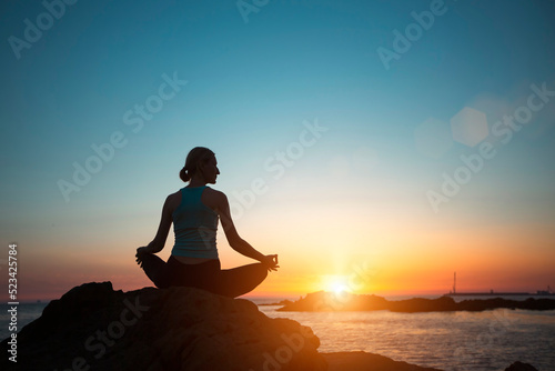 A woman does yoga, meditating on an ocean beach during a beautiful sunset.
