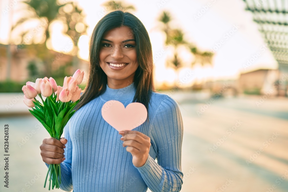 Beautiful hispanic woman holding tulips bouquet and pink heart at the city Beautiful hispanic woman holding tulips bouquet and pink heart at the city