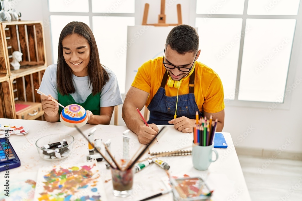Young hispanic couple smiling happy drawing sitting on the table at art studio.