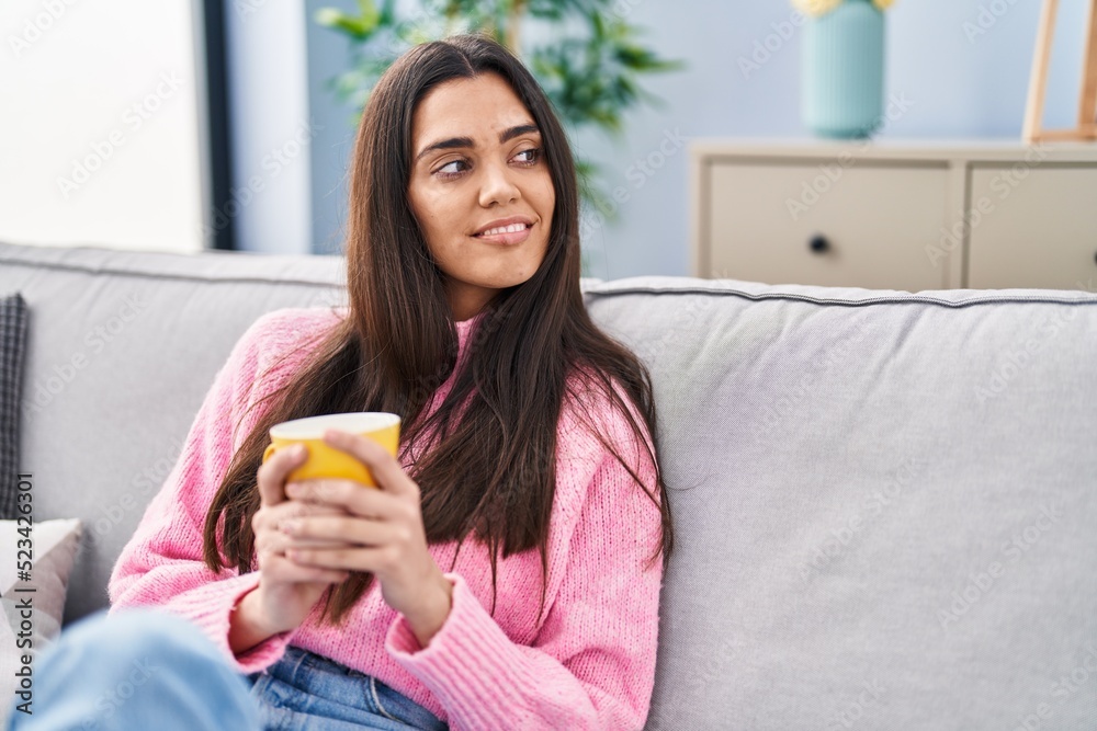 Young hispanic woman drinking coffee sitting on sofa at home Young hispanic woman drinking coffee sitting on sofa at home