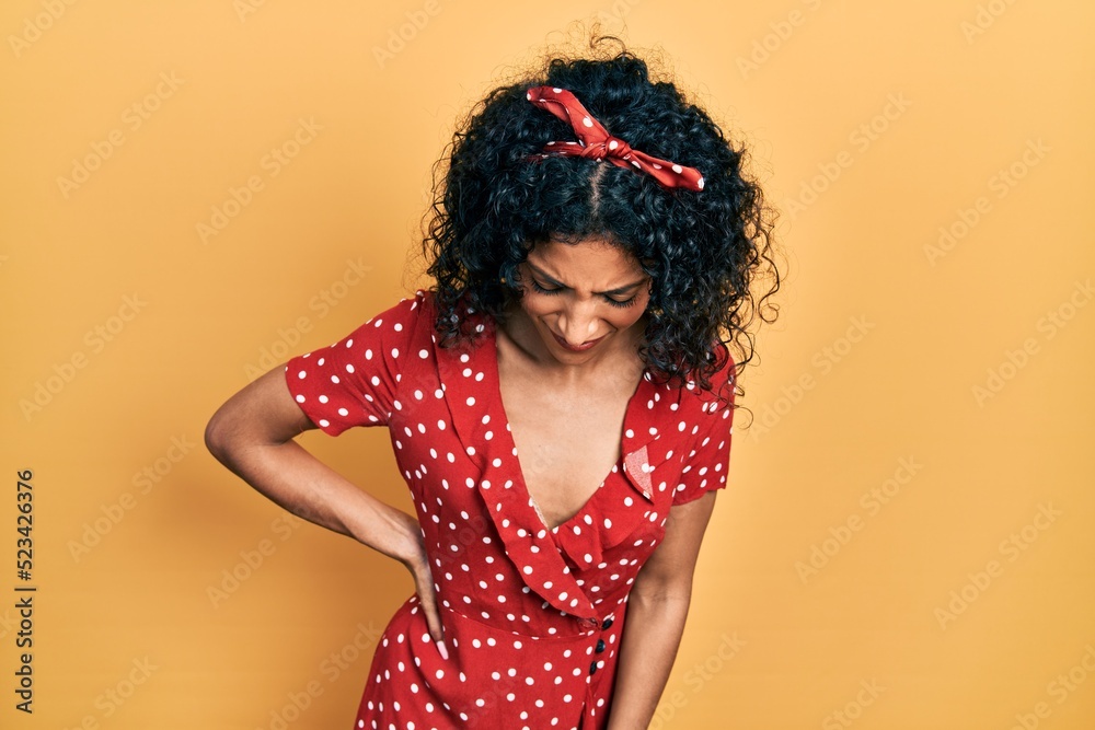 Young latin girl wearing summer dress suffering of backache, touching back with hand, muscular pain Young latin girl wearing summer dress suffering of backache, touching back with hand, muscular pain