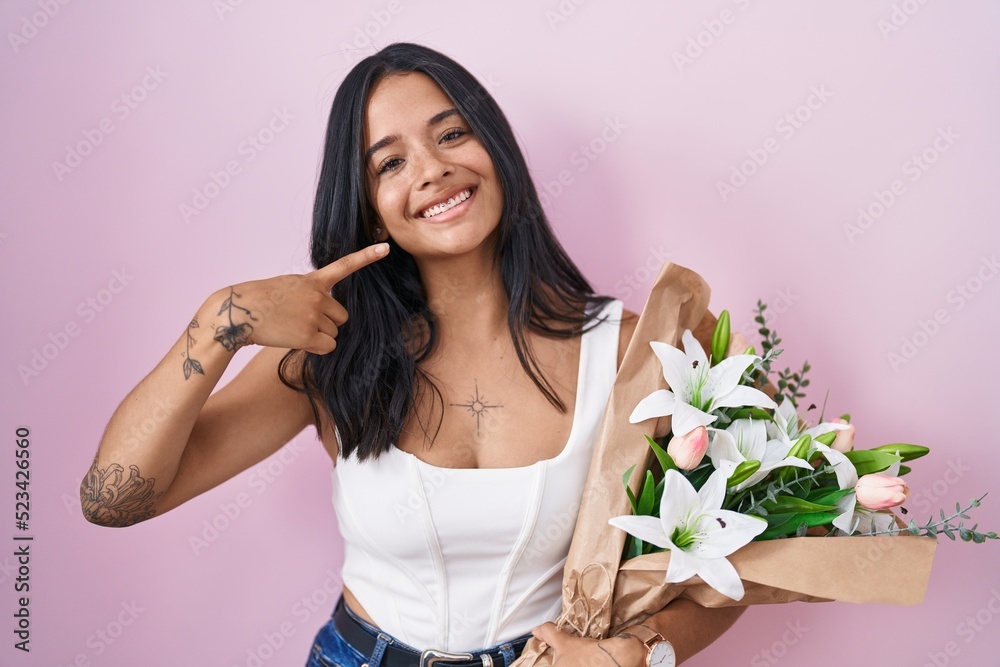 Brunette woman holding bouquet of white flowers smiling cheerful showing and pointing with fingers teeth and mouth. dental health concept. Brunette woman holding bouquet of white flowers smiling cheerful showing and pointing with fingers teeth and mouth. dental health concept.