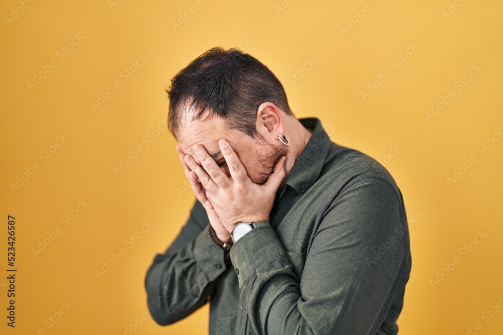 Plus size hispanic man with beard standing over yellow background with sad expression covering face with hands while crying. depression concept. Plus size hispanic man with beard standing over yellow background with sad expression covering face with hands while crying. depression concept.