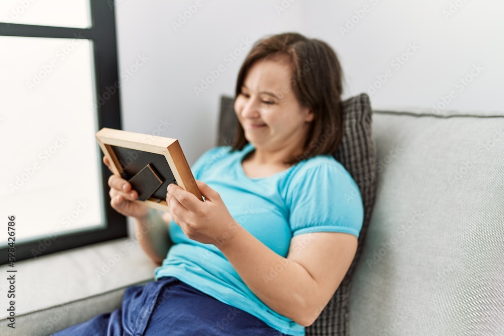 Brunette woman with down syndrome sitting on the sofa looking at frame at the living room Brunette woman with down syndrome sitting on the sofa looking at frame at the living room