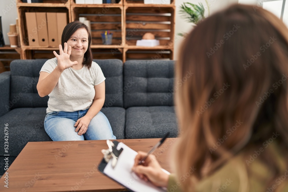 Hispanic girl with down syndrome doing therapy showing and pointing up with fingers number five while smiling confident and happy. Hispanic girl with down syndrome doing therapy showing and pointing up with fingers number five while smiling confident and happy.