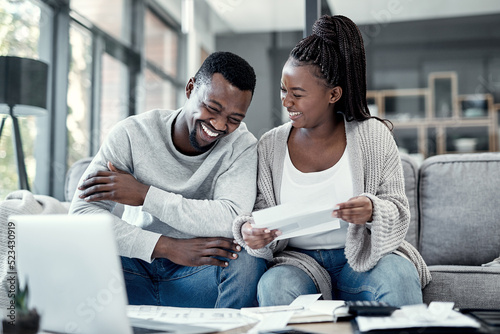 Happy black couple paying bills on a laptop at home, checking their budget and savings. Smiling African american husband and wife enjoying future planning, excited about an investment and good credit photo