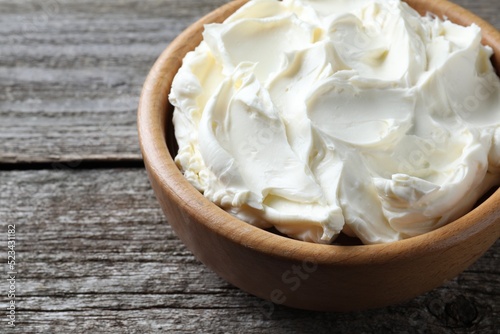 Bowl of tasty cream cheese on wooden table, closeup