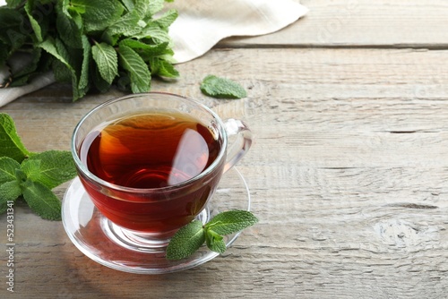 Cup of hot aromatic tea with mint on wooden table. Space for text