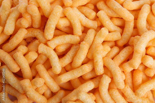 Many tasty cheesy corn puffs as background, top view