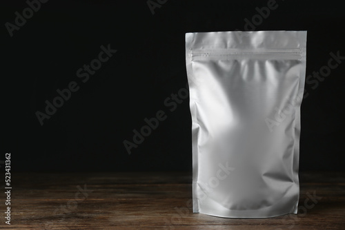 One blank foil package on wooden table against dark background. Space for text