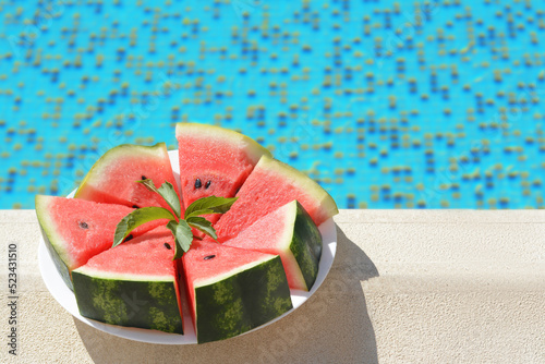 Slices of watermelon on white plate near swimming pool outdoors. Space for text