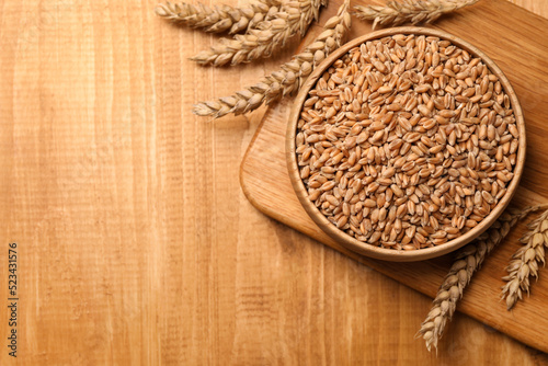 Wheat grains with spikelets on wooden table, flat lay. Space for text