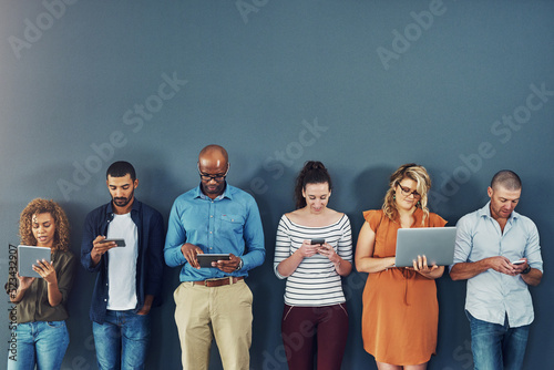 A group of people distracted due to the overuse of technology against gray studio background. Many employees are addicted and obsessed with social media with a dependence on gadgets or devices photo