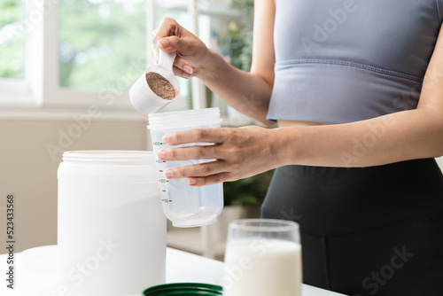 Young sporty woman pouring protein powder into a cup to make replacement food meal after workout photo