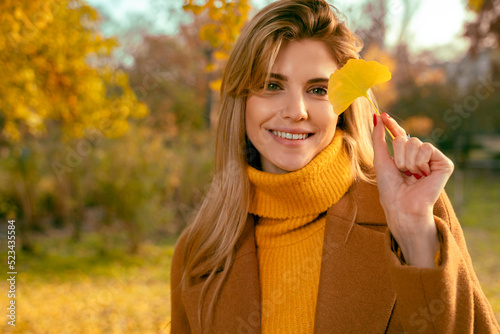 Portrait of charismatic young blonde in sweater holding leaf and smiling 