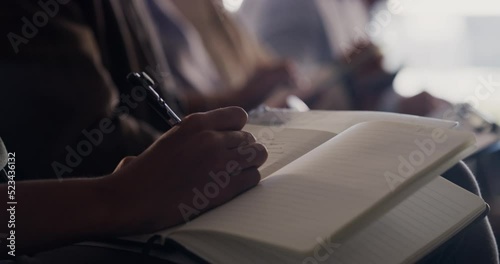 Audience taking notes at a conference, convention or business trade show sitting in a row, attending a presentation. Corporate men and women attending a company meeting, training event or seminar