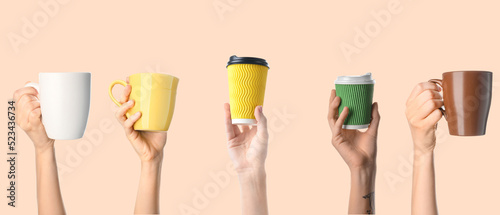 Hands with cups of coffee on beige background