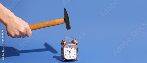 Hand with hammer and alarm clock on blue background